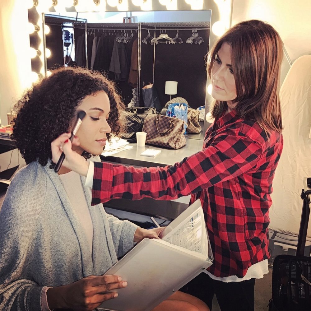 Shira applying makeup on a model backstage at a television studio